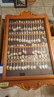 Full view of the wooden spoon rack with glass containing rows of assorted collectible souvenir spoons.