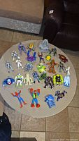 Top-down view of all figurines arranged on a round beige table, showing variety of characters including Buzz Lightyear, Spider-Man, and others.