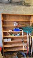 Full frontal photo of the wooden shelving unit showing five shelves with various small items stored on it. Located in a garage with concrete block wall background.