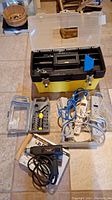 Photo showing yellow Stanley toolbox open with screwdriver/ratchet bit set, four power extension cords, and Black & Decker corded drill