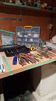 Photo showing assortment of hand tools laid out on workbench with carry case and drill bits organizer visible behind