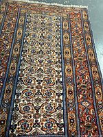 Photo showing the full length and width of the rectangular Birjand rug with visible intricate floral patterns on cream field and rust colored borders.