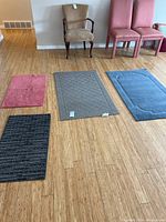 Four area rugs on wood floor: pink, gray, blue, and black, showing size and texture detail.