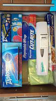 Top-down view of kitchen drawer showing assorted boxes of Ziploc bags, Reynolds Wrap aluminum foil, Cut-Rite wax paper, parchment paper, and a plastic wrap dispenser.