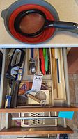 Photo of two kitchen drawers containing assorted knives, sharpening tool, wooden spoons, spatulas, strainers, and cheese shredder organized in their compartments.