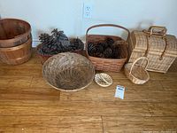 Full view of all baskets arranged on wooden floor including bushel basket, woven baskets and a picnic-style basket with clasp.