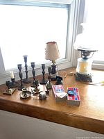 View of the main collection showing 6 brass candle holders of different types, a small lamp with fabric shade, and two boxes of matches.