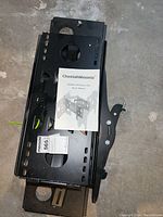 Top view of the CheetahMounts wall mount with the manual placed on top, showing the heavy-duty metal bracket with multiple mounting holes and slots.