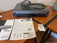 Full front view of the Cinevision DVR1000 player on a wooden surface with remote control and user guide sheets placed beside it.