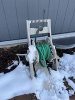 Plastic hose reel cart with green hose coiled, some snow around and on it, positioned against house siding.