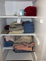View of shelves with assorted linens including folded blankets, sheets, and a small coffee maker or similar appliance, with tags visible
