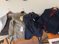 Four men's suit jackets laid out partially overlapping showing interior linings and exterior fabric.
