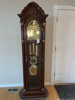 Full view of the tall wooden grandfather clock with glass front door and pendulum visible inside.