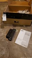 Samsung DVD and VHS combo player in open box with two remotes and instruction manual on floor.