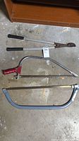 Photo showing three hand saws and one pair of garden clippers laid on concrete floor.
