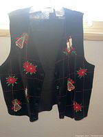 Black holiday-themed sleeveless sweater vest with embroidered poinsettias and bells