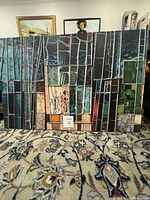 Front view showing three tempered glass panels with abstract art geometric design in varied dark shades and earth tones; panels positioned on carpeted floor in interior room.