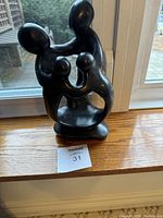 Black hand carved abstract sculpture of a family of four with rounded forms and a smooth finish, positioned on a wooden window sill.