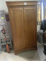 Front view of wooden armoire showing two paneled doors with wooden knobs, crown molding on top and decorative base trim.