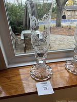 One etched crystal hurricane candle holder on a windowsill showing full height, etched pattern, and weighted base; second holder partially visible