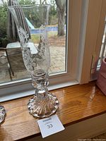 Single clear etched crystal hurricane candle holder on wooden sill with window background