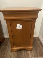 Front view of the solid wood bedside table with a single door closed, showing the decorative molding and metal knob.