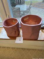Two pink ceramic flower pots shaped like crumpled paper bags placed on a window sill, showing front and side views.