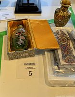 Photo of Chinese glass snuff bottle in rectangular yellow fabric-lined case with floral interior painting and part of mandela patterned printed item visible