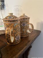 Two Chinese ceramic tea mugs with lids and infusers, decorated with yellow floral and vine patterns.