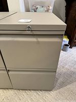 Front view of beige metal file cabinet showing two drawers and lock with key on the top drawer.