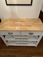 Front view of the white kitchen cart showing 2 drawers with metal handles, wine bottle storage slots below, and open shelving on sides.