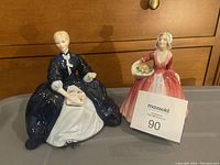 Both Royal Doulton figurines together, Laurianne in navy/white and Janet in red/white, each seated with their respective props.