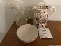 Clear glass pitcher with star medallion pattern, mason's patent ironstone ceramic floral pitcher, and plain ceramic bowl on a wooden surface