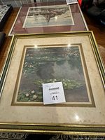 Framed water lilies art print on a table with gold frame and visible artist signature.