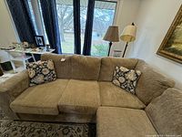 Front view of entire L-shaped sectional couch with two floral throw pillows on one side