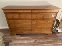 Front view of solid wood dresser showing eight drawers with metal knobs, natural wood finish and curved bottom edge.