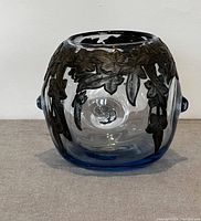 Full view of the pale blue cylindrical glass vase with dark metal floral overlay wrapping around the sides.