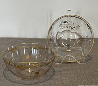Pair of clear glass antique bowls with gold leaf trim and intricate gold embellishments on sides and rim, photographed on neutral surface with one bowl on a stand.