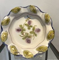 Full view of the pottery dish showing the scalloped edge with green leaves and central floral and bee design.