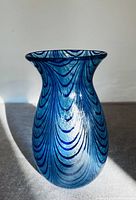 Front view of a blue iridescent glass vase showing wave-like dark blue lines with light reflecting off the surface.