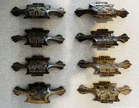 Set of eight handcarved antique wooden dresser handles laid out on a fabric surface, showing the front and top views with detailed symmetrical carvings and dark wood patina.
