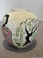 View of the vase showing a hand-painted female figure in pink traditional clothing standing beside a tree with green willow leaves. The glaze has a visible crackled texture.