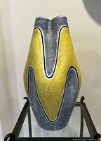 Full front view of the vase showing the yellow and blue abstract design with black outlining and the top rim shaped with two peaks.