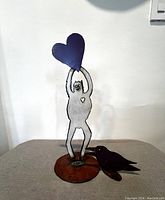 Front view of Heartman figure holding blue heart with black bird on rust-colored base
