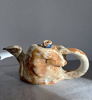 Side view of the teapot showing the handle, spout, and beaded lid