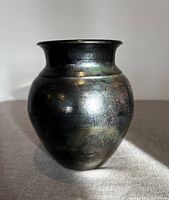 Front view of rounded black Raku vase with iridescent subtle color highlights and flared lip.