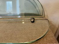 Close-up of glass shelf edge with small chrome metal support underneath for mounting.