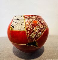 Side view of the rounded pottery showing cracked ceramic shards in red, white and floral patterns with gold seams