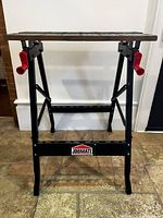 Front view of the Jobmate workmate workbench showing black metal frame, red handles, and wooden top boards.