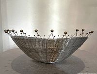 Side view of wire basket showing shallow bowl shape and wire construction with brass/bronze knob accents on rim